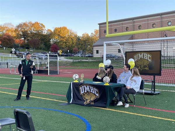High School senior Sara Gavagan, Athletic Director John Buonamano and others sitting at table on soccer field
